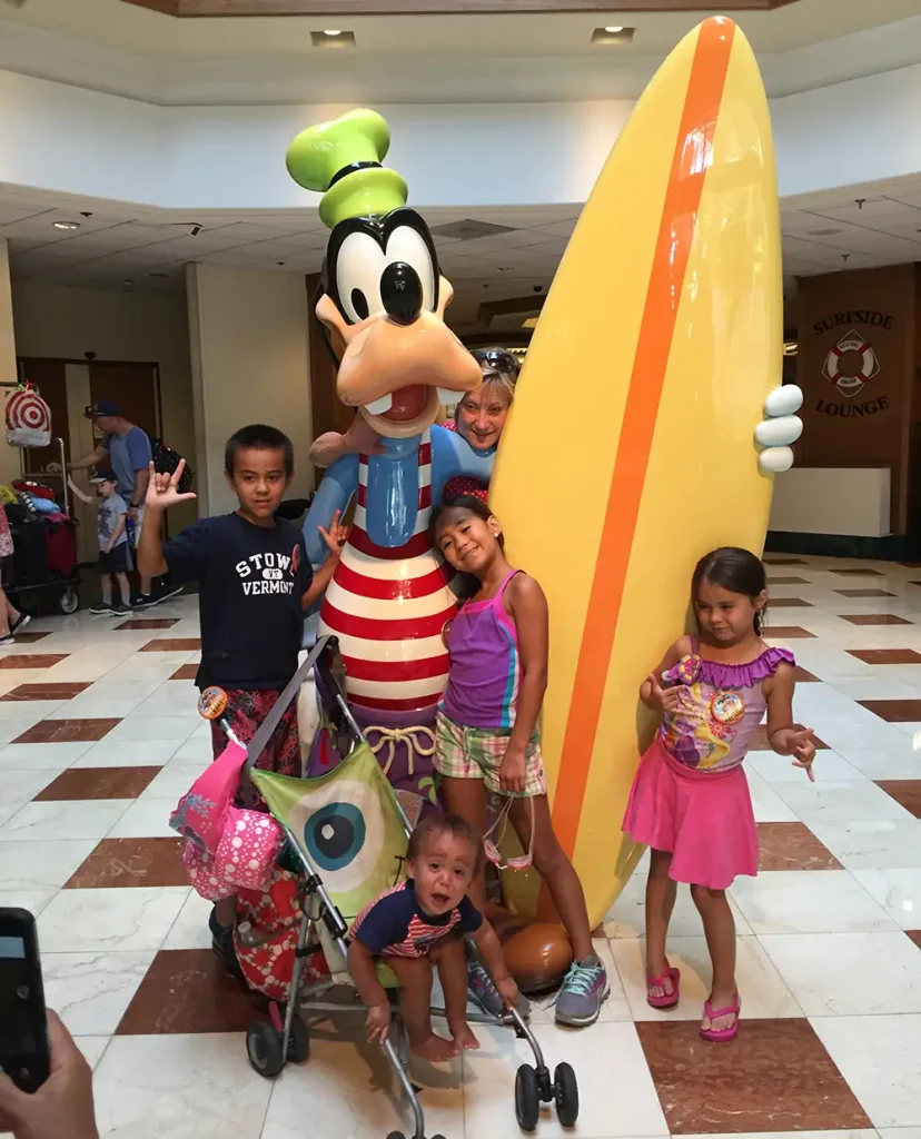 Favorite Grampy's grandkids standing with Goofy holding a surfboard.